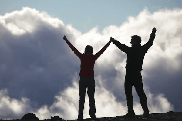 two silhouettes of a man and woman holding hands and raising them as if in victory with clouds in front of them