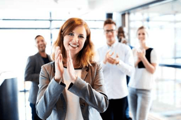woman in front clapping with four blurred coworkers clapping behind her
