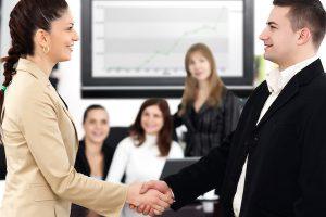 Business professionals in office space and man and woman are shaking hands in forefront