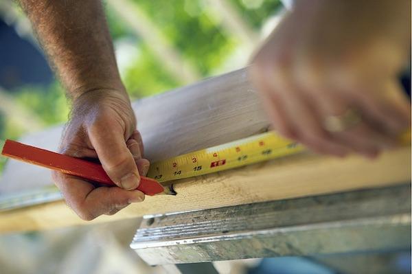 carpenter measuring board with tape measure and marking it with carpenter pencil