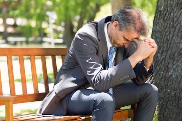 man on bench with head in hands looking hopeless