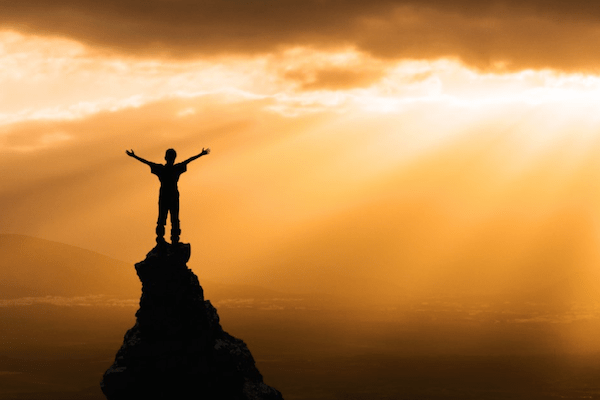 silhouette of person standing on mountaintop with arms raised