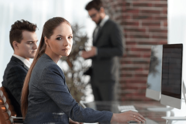 business woman looking away from her computer with disgust or anger while two business men are in the background