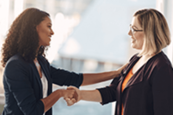 two women smiling with compassion as they shake hands