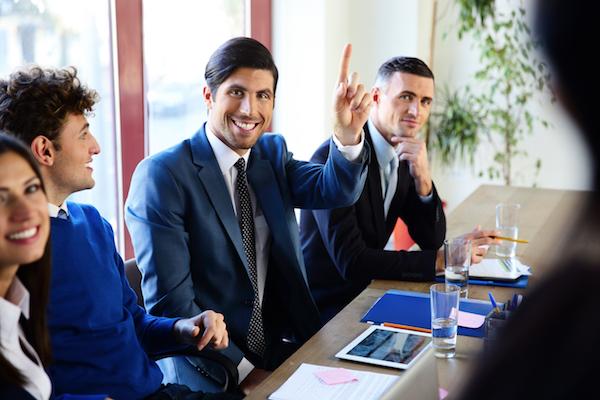 business people at conference table where one has big smile and raised his fingers