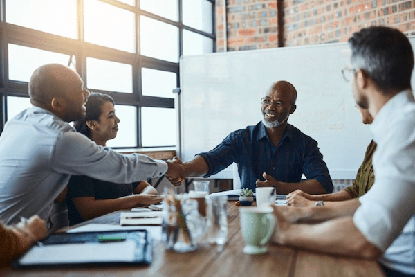 professionals around conference table while two men shake hands