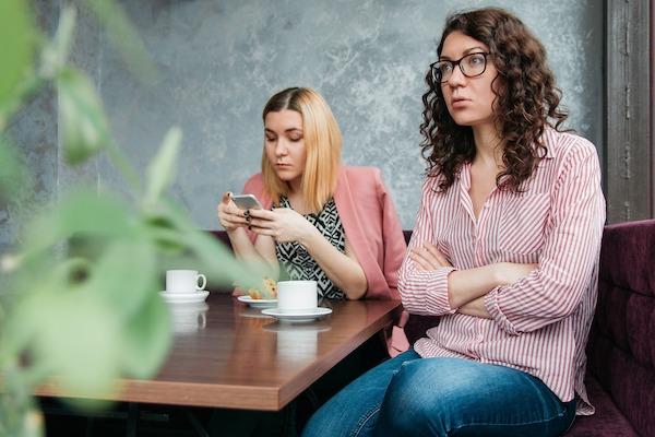 one woman looks upset while another focuses on her cell phone