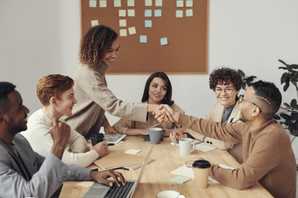 professionals around a conference table with man and woman shaking hands