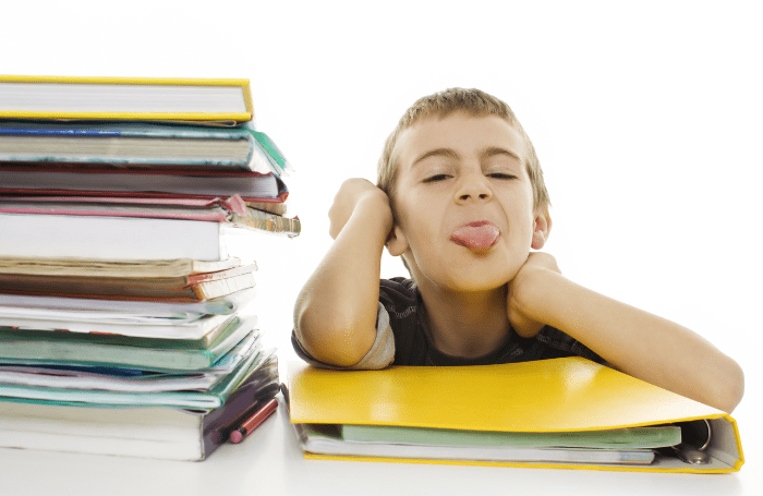 boy student sticking out tongue by stack of books