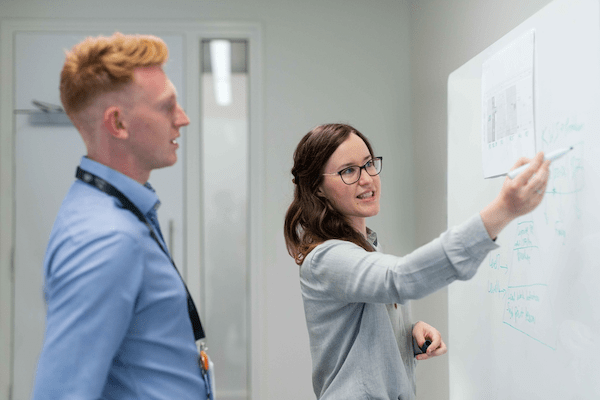 woman writing on white board with male co-worker looking on