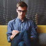 man sitting on couch writing in book or notepad