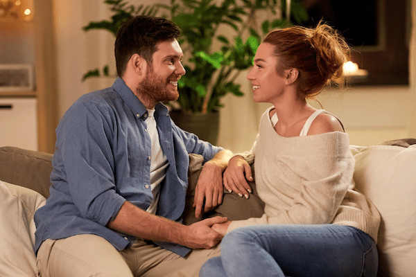 man and woman holding hands and gazing lovingly while on couch