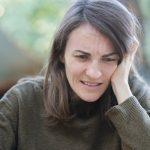 woman with grimace and hand on head looking stressed