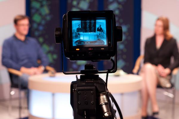 video camera in front of man and woman talking in a studio